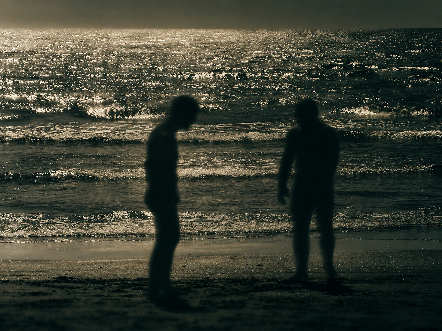 Two blurred figures on a beach in Procida facing a bright sea